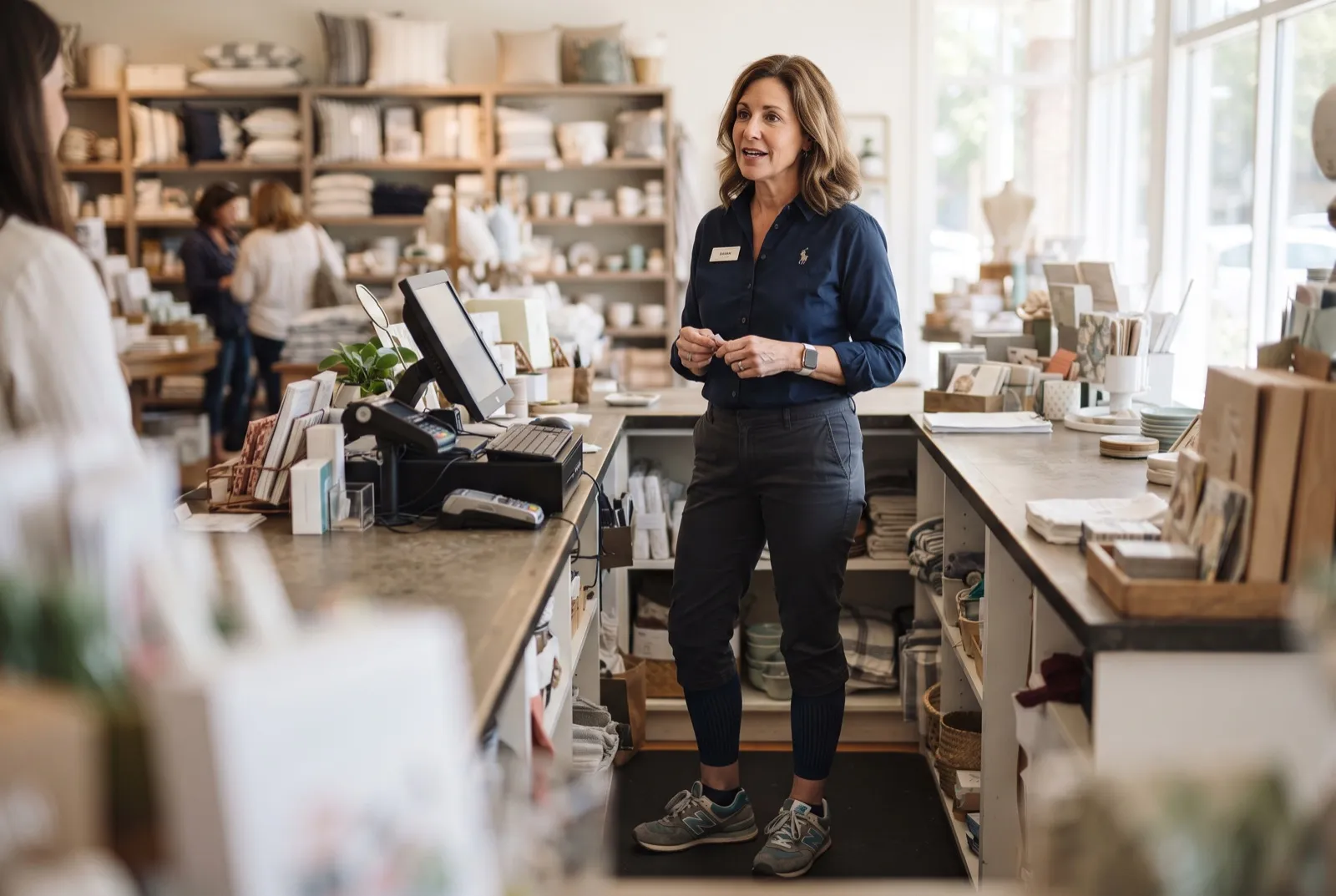 A retail worker in her 40s standing behind a store counter, wearing dark compression socks with comfortable sneakers